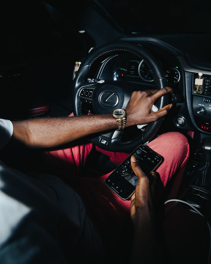 Driver holding smartphone inside luxury car at night in Lagos, Nigeria.